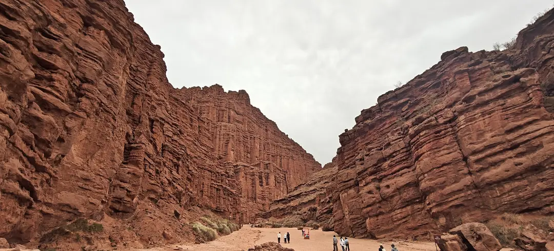 Visitors dwarfed by the towering, layered red cliffs of Wensu Grand Canyon