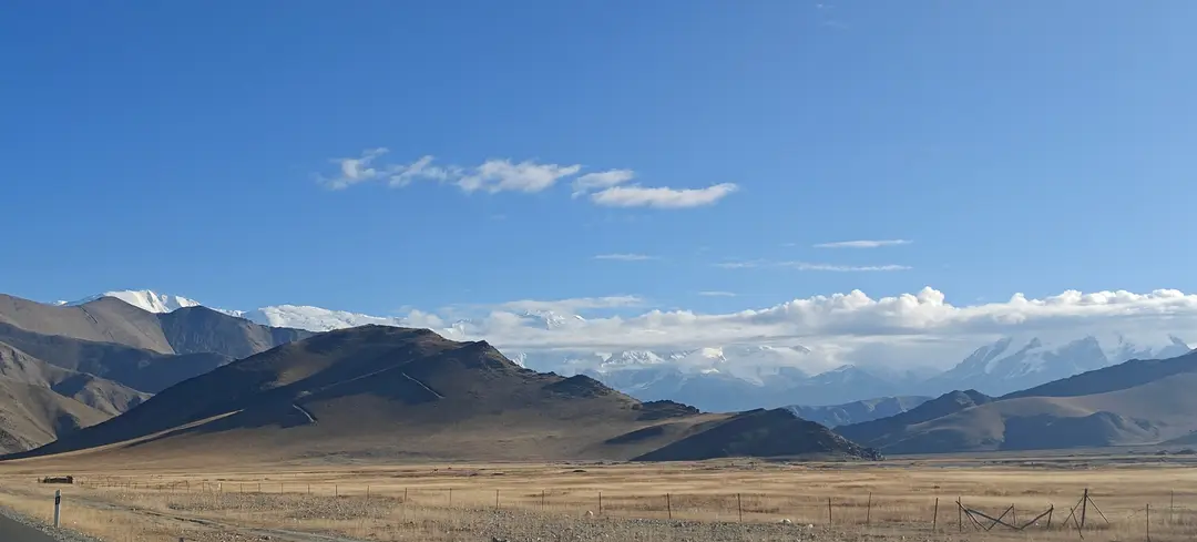 Pale grassland and brown ridges below snow peaks rising through clouds on the Pamir Plateau